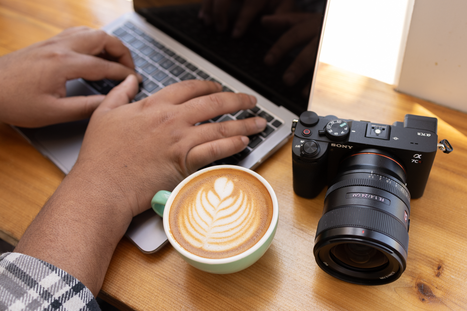 hands typing on laptop keyboard next to a latte and a camera